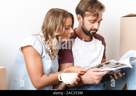 Foto der kaukasischen Paar Kaffee trinken und lesen Magazin beim Sitzen in der Nähe von Kartons über weiße Wand isoliert Stockfoto
