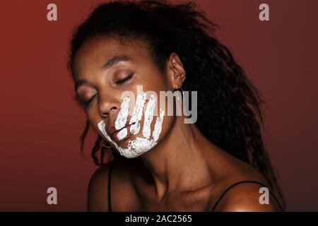 Nahaufnahme eines jungen afrikanischen Frau mit weißen Hand Druck auf ihr Gesicht über den roten Hintergrund isoliert Stockfoto