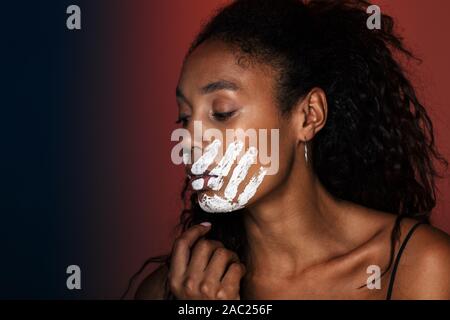 Nahaufnahme eines jungen afrikanischen Frau mit weißen Hand Druck auf ihr Gesicht über den roten Hintergrund isoliert Stockfoto