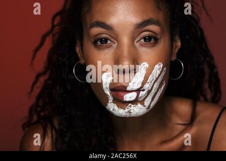 Nahaufnahme eines jungen afrikanischen Frau mit weißen Hand Druck auf ihr Gesicht über den roten Hintergrund isoliert Stockfoto