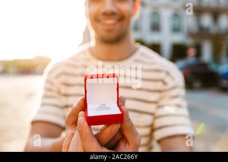 Bild von fröhlichen maskulinen Mann und lächelnd Geschenkkarton mit Ring, während Wandern in der Stadt. Stockfoto