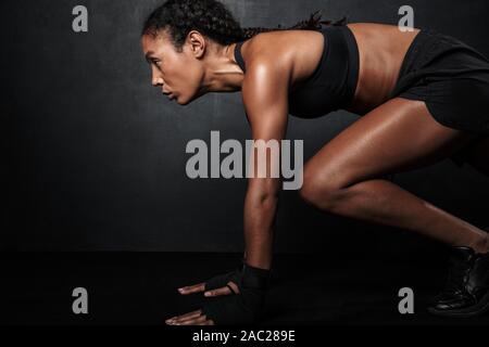 Bild der muskulöse afrikanische amerikanische Frau in Sportkleidung hocken, während Sie trainieren über schwarzen Hintergrund isoliert Stockfoto