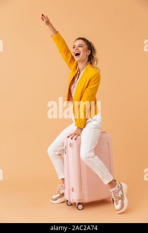 Bild von positiv optimistisch emotionale Frau Touristen sitzen auf Koffer über beige Wand Hintergrund isoliert. Stockfoto