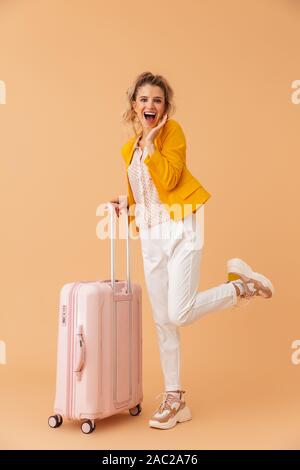 Bild von positiv optimistisch emotionale Frau Tourist mit Koffer über beige Wand Hintergrund isoliert. Stockfoto