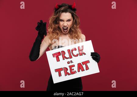 Bild von Frechen Frau Daemon in Karneval Kostüm über rote Wand Hintergrund Holding copyspace leer mit Halloween Trick oder Text behandeln isoliert. Stockfoto