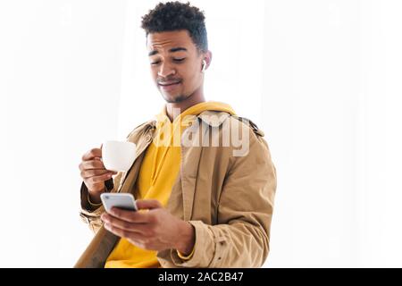 Bild von überrascht african american Guy holding Smartphone und Kaffee Tasse in Weiß studio Stockfoto