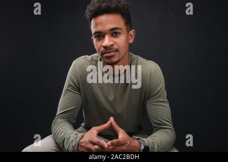 Bild von zuversichtlich african american Guy auf Kamera während der Sitzung über schwarzen Hintergrund isoliert Stockfoto