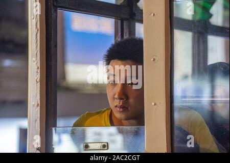 Ein junger Mann schaut aus dem Fenster der Straßenbahn im Zentrum von Hong Kong Stockfoto