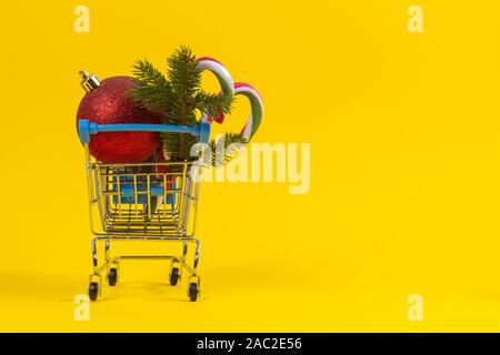 Mini Warenkorb mit Weihnachten Dekoration Christbaumkugeln, Fir Tree Branch und Zuckerstangen auf gelbem Hintergrund Stockfoto