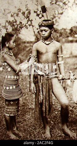 30Er vintage Foto von zwei Kindern aus dem Dyak (aka Dayuh) native Stamm Menschen von Borneo (Iban oder Meer Dajak Junge und Mädchen in traditioneller Kleidung) Stockfoto