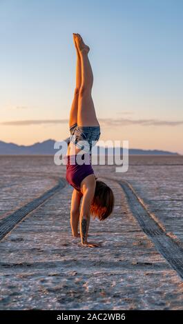 Schöne Frau macht Handstand während des Sonnenuntergangs in der Bonneville Salt Flats Stockfoto