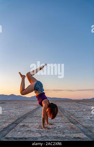 Schöne Frau macht Handstand während des Sonnenuntergangs in der Bonneville Salt Flats Stockfoto