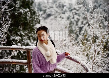 Eine junge Chinesin Posen für Fotos im Schnee mit der Jingshan Park nach dem ersten Schneefall in diesem Winter in Peking, China, am 30. November, 2019. Werden Stockfoto