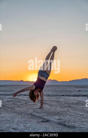 Schöne Frau macht Handstand während des Sonnenuntergangs in der Bonneville Salt Flats Stockfoto