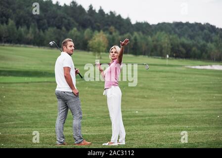Frau, etwas hinter sich. Paar Golfspieler mit Stöcken in den Händen stehen auf dem Rasen