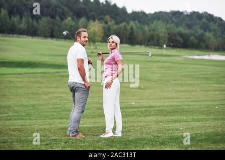 Zurück zu schauen. Paar Golfspieler mit Stöcken in den Händen stehen auf dem Rasen
