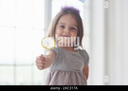 Kleines Mädchen mit gelben Candy in Ihrer rechten Hand auf weißem Hintergrund Stockfoto