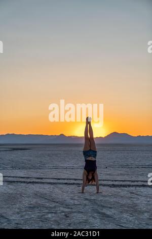 Schöne Frau macht Handstand während des Sonnenuntergangs in der Bonneville Salt Flats Stockfoto