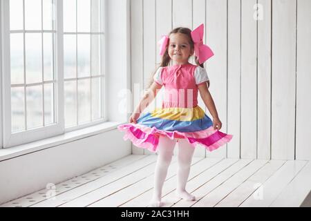 Dieses Mädchen hat schönes Kleid. Kind stand neben den Fenstern im weißen Raum und für ein Foto posieren Stockfoto