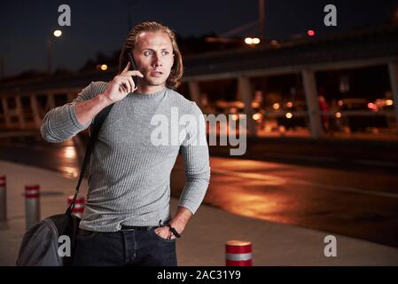 Angespannt. Junge stilvollen Mann zu Fuß durch die Nacht Street in der Nähe der Straße und ein Gespräch am Telefon Stockfoto