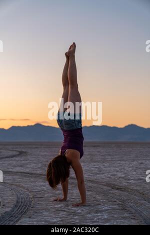 Schöne Frau macht Handstand während des Sonnenuntergangs in der Bonneville Salt Flats Stockfoto