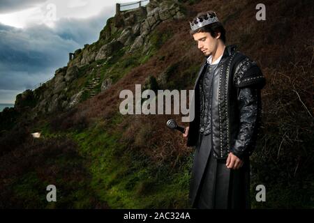Stattlicher König mit Schwert steht in Kontemplation mit Hill und Teile von im Hintergrund das Schloss Stockfoto