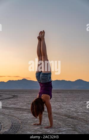 Schöne Frau macht Handstand während des Sonnenuntergangs in der Bonneville Salt Flats Stockfoto