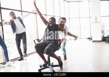 Die Jugendlichen Spaß in der spacey Büroraum, die afro-amerikanische Oman auf dem Stuhl Stockfoto