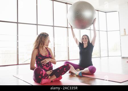 Schwangere Frau saß auf dem Fitness Matte und halten grosse Stabilität Kugel, während Sie auf den Freund Stockfoto