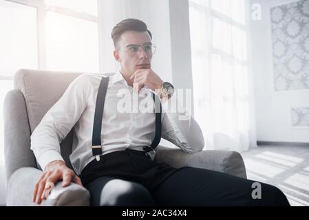 Große Zimmer. Schön sehen sie auf der Hand. Nahaufnahme Foto von attraktiven Kerl in die Gläser und stilvolle Verschleiß auf dem Stuhl Stockfoto