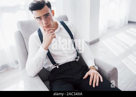 Schauen Sie oben. Nahaufnahme Foto von attraktiven Kerl in die Gläser und stilvolle Verschleiß auf dem Stuhl Stockfoto