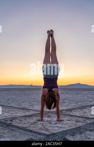 Schöne Frau macht Handstand während des Sonnenuntergangs in der Bonneville Salt Flats Stockfoto