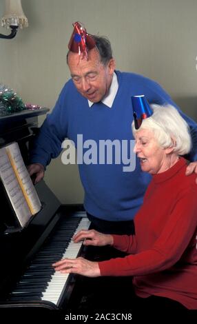 Senior Paar in Partei Hüte in Singen Song um Piano an Weihnachten Stockfoto