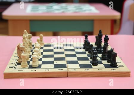 Holz- Schachfiguren und Schachuhr auf einem rosa Hintergrund. Holz- Schachfiguren auf dem Schachbrett. Intellektuelles Spiel Stockfoto
