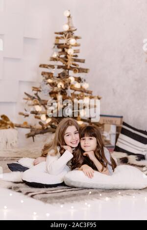 Zwei lächelnde Mädchen in der Nähe von Weihnachten neues Jahr Komposition. Festliche Holz- Baum mit Spielwaren, Geschenke eingerichtet, Bälle. Winterurlaub Konzept. Stockfoto