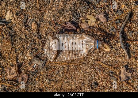 Eine zerdrückte und zerknittert aus klarem Kunststoff Flasche Wasser am Strand am See schmutzig und bedeckt mit Sand an einem sonnigen Tag im Herbst Stockfoto