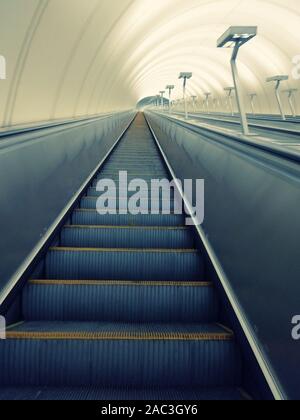 Abstieg in den Tunnel Stereo-Rolltreppe Treppe Licht von unten. Moderne Tunnel Rolltreppe elektronisches System bewegt Vintage-Stil, mechanisch Stockfoto