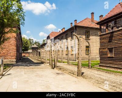 Oświęcim, Polen - Juni 05, 2019: elektrischen Zaun mit Stacheldraht und Ziegel Gefängnis Gebäuden im Konzentrationslager Auschwitz-Birkenau in Oświęcim, Stockfoto