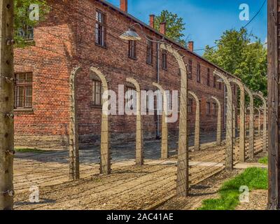 Oświęcim, Polen - Juni 05, 2019: elektrischen Zaun mit Stacheldraht und Ziegel Gefängnis Gebäuden im Konzentrationslager Auschwitz-Birkenau in Oświęcim, Stockfoto