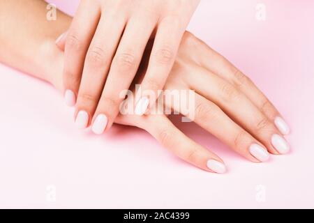 Der weibliche Hände mit klassischen Pastelltönen Maniküre auf rosa Hintergrund. Beauty Salon. Stockfoto