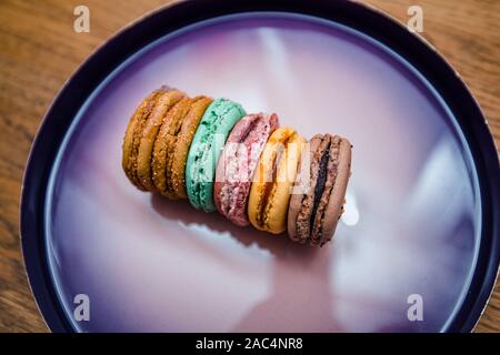 Seitenansicht des köstlichen bunten authentische französische Macarons von organischen Inhaltsstoffen auf Luxus violett Platte bereit zu essen. Stockfoto