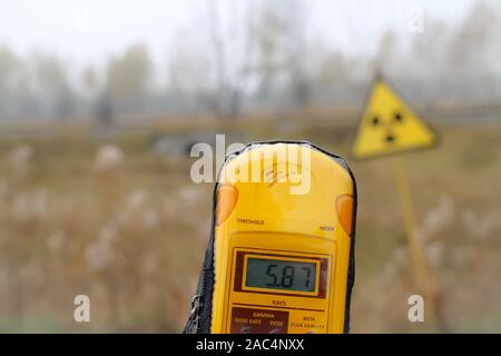 Ein Dosimeter ist vor der Radioaktivität Warnschild gehalten, 5,87 Millisievert pro. Stadt Pripyat, Sperrzone von Tschernobyl, Ukraine. Stockfoto