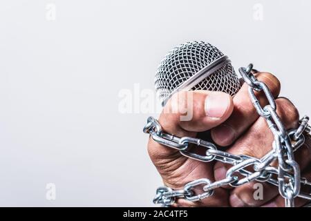 Hand mit Mikrofon und Kette auf Faust Hand auf weißem Hintergrund, Tag der Menschenrechte Konzept Stockfoto