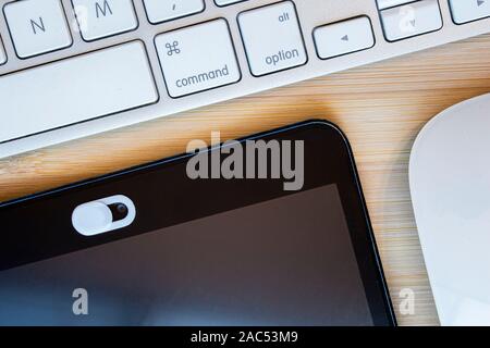 Eine weiße Farbe kamera Privatsphäre abdecken. Schieben Sie die Webcam. Abdeckung für ein elektronisches Gerät mit einer Tastatur an einem hölzernen Tisch Stockfoto