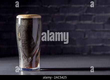 Eine dunkle Irische trocken Stout Bier Glas mit einem schwarzen Stein auf dem Hintergrund Stockfoto