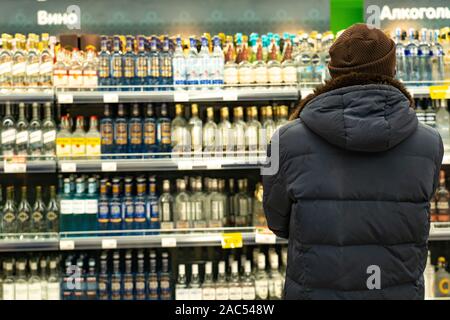 Jekaterinburg, Russland - November 2019. Ein Mann in Vor der Zeilen von Spiritus in einem Supermarkt. Eine große Auswahl an alkoholischen Getränken. Die Stockfoto