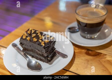 Fudgy reichen dunklen Schokolade Kuchen auf Platte mit Kaffee und Löffel Stockfoto