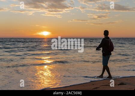 Mann mit Angelrute steht auf sandigen Strand bei Sonnenuntergang in Goa, Indien Stockfoto