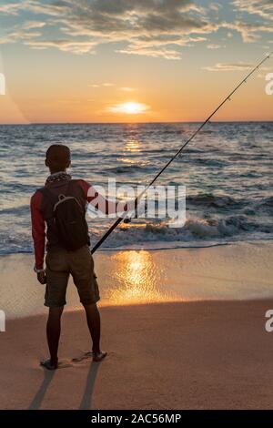 Mann mit Angelrute steht auf sandigen Strand bei Sonnenuntergang in Goa, Indien Stockfoto