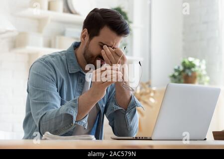 Müde junge Mann fühlen, um eine Überanstrengung der Augen halten Gläser ermüdet vom Computer Stockfoto